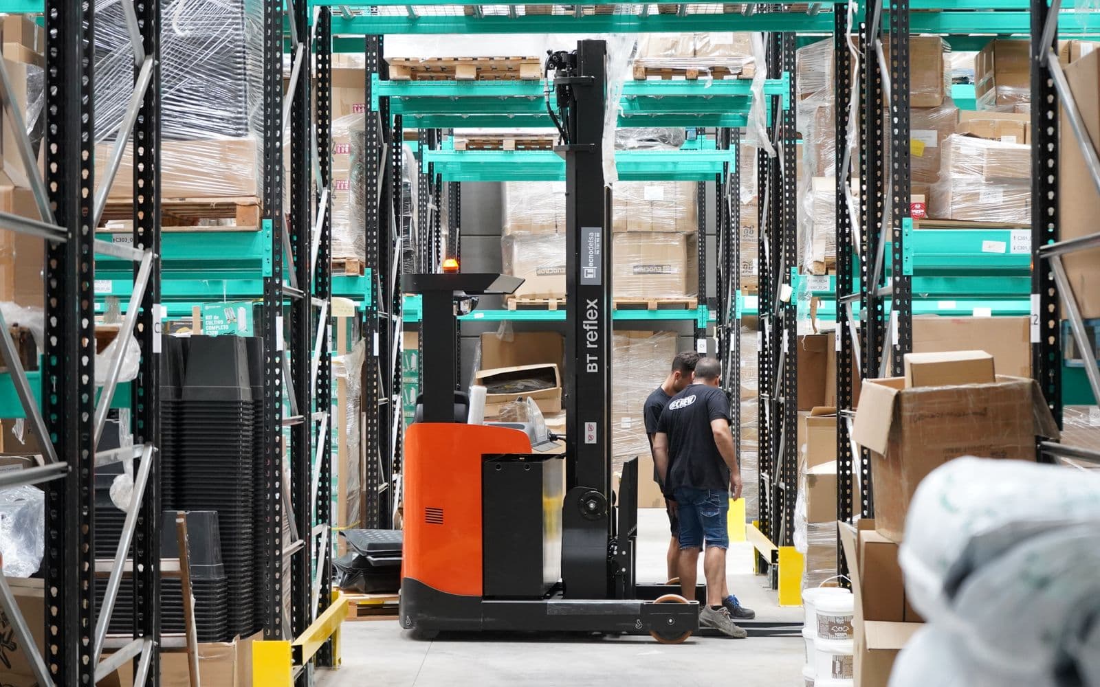 Warehouse workers and a forklift in a storage aisle