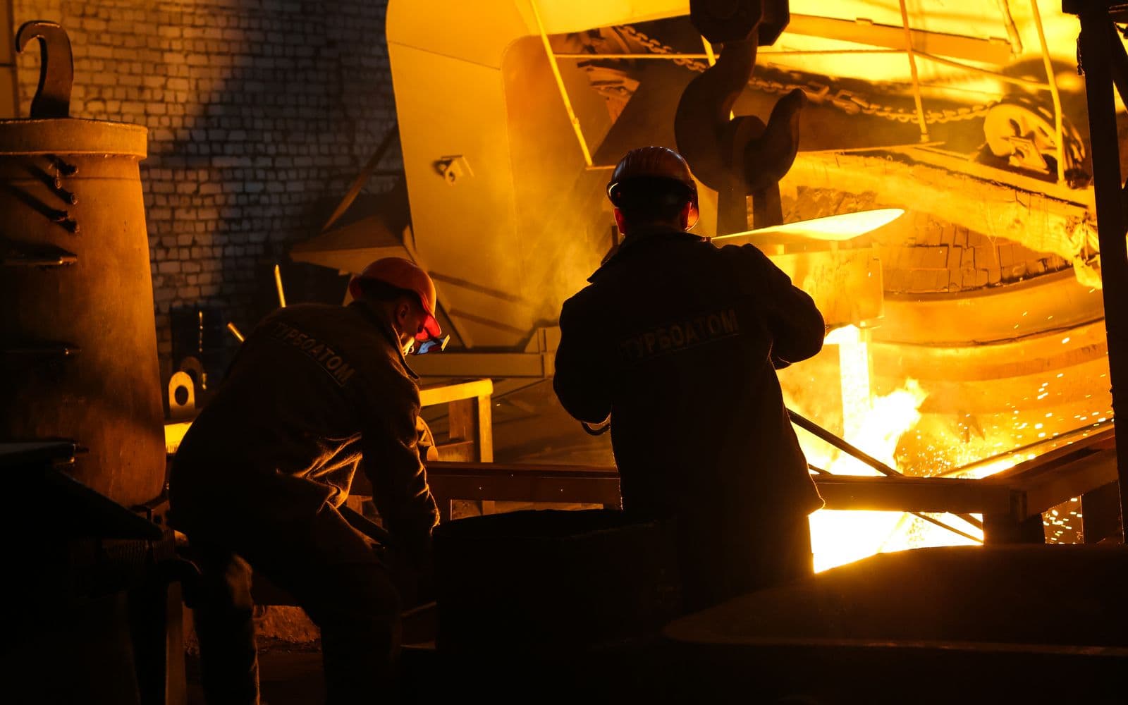 Workers in protective helmets operating beside a glowing steel furnace